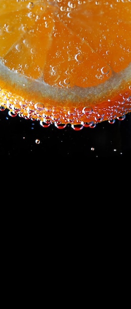 Cut round a piece of orange orange in bubbles of carbonated water on black background abstract background vertical image of free space to text summer freshness vitamins healthy diet food