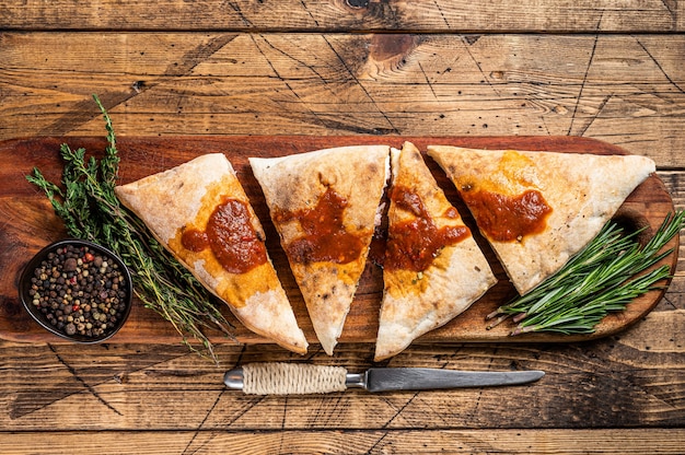 Cut and sliced Calzone closed pizza with ham and cheese on wooden board with hot tomato sauce. wooden background. Top view.