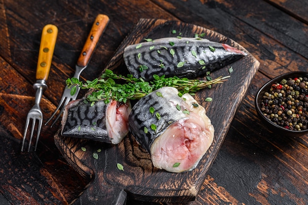 Cut smoked mackerel fish with herbs. Dark wooden background. Top view.