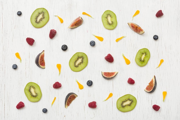 Cut summer fruit figs kiwi raspberries blueberries and flower petals on wooden background