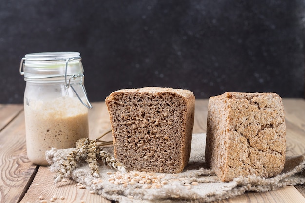 写真 スターターのスペルト小麦の小麦粉のパンを半分に切り、天然木の背景のマットの端にあります