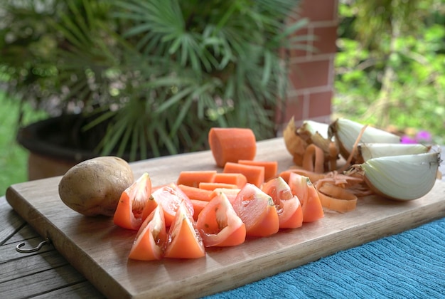 Cut tomatoes carrot onions and potatoes on wooden chopping board