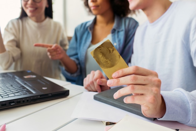 Cut view of a guy that is holding a credit card in his hands while he is looking at laptop with girls together.