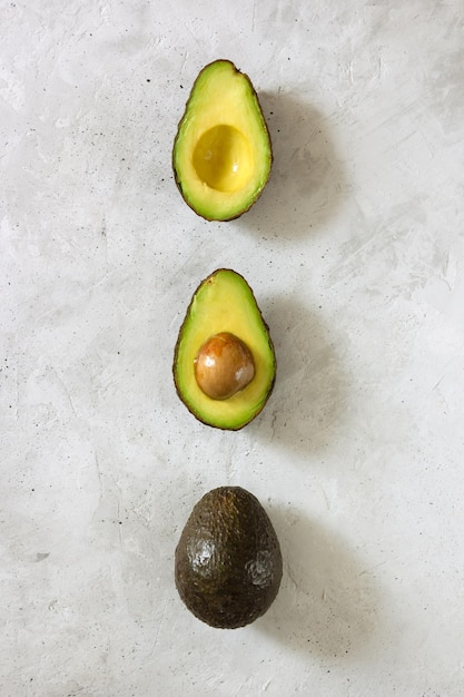 Photo cut and whole avocado laying on a vertical line on the gray table top view