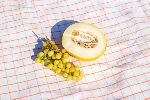 Cut yellow melon, grapes on the tablecloth. Top view, flat lay.