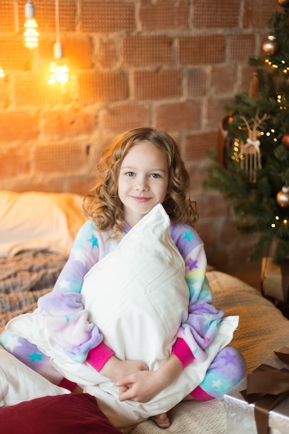 Photo cute 10 year old girl sitting on the bed and hugging pillows