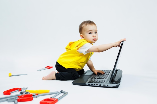 A cute 2yearold boy is sitting at a digital laptop on a white background Child and modern portable computer gadget