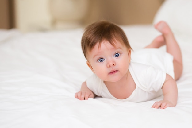 집에서 하얀 침구를 입은 귀여운 3개월 아기 소녀가 카메라를 잘 보고 있습니다.