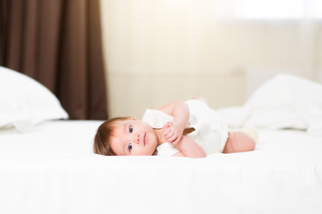 A cute 3 month baby girl in white bedding at home look nice at camera