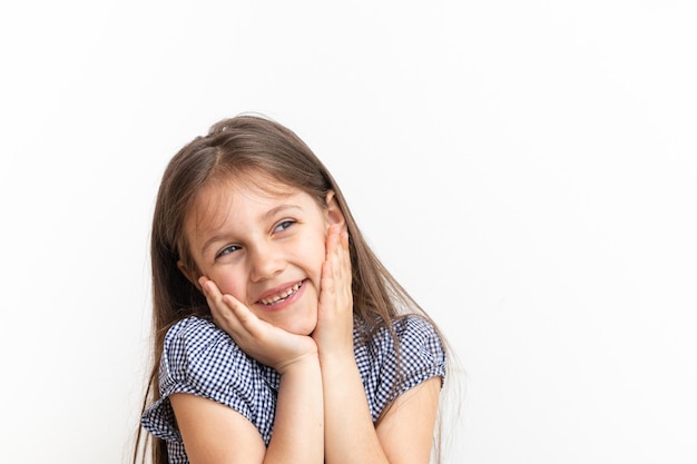 Cute 7 year old girl with long hair smiles holding hands on face and not looking at camera