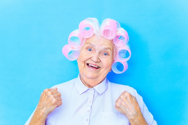 ブルー スタジオの背景で幸せそうに見えて白い髪にカーラーでかわいい 80 歳の女性