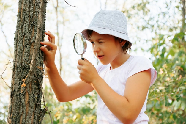 Cute adorable Caucasian girl kid looking at tree in forest through magnifying glass Children friends siblings with loupe studying learning nature outside Child education concept