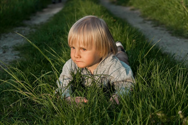 Cute adorable little caucasian kid toddler boy having fun lying on green grass lawn at home yard gardenChild on lawn in backyard during sunsetHappy childhoodchildren's healthcare serenity concept