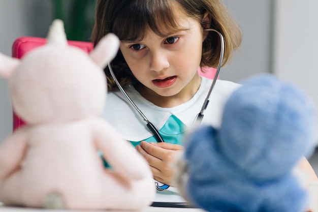 Carina adorabile bambina in età prescolare indossa un'uniforme medica che tiene in mano uno stetoscopio che ascolta un paziente giocattolo malato