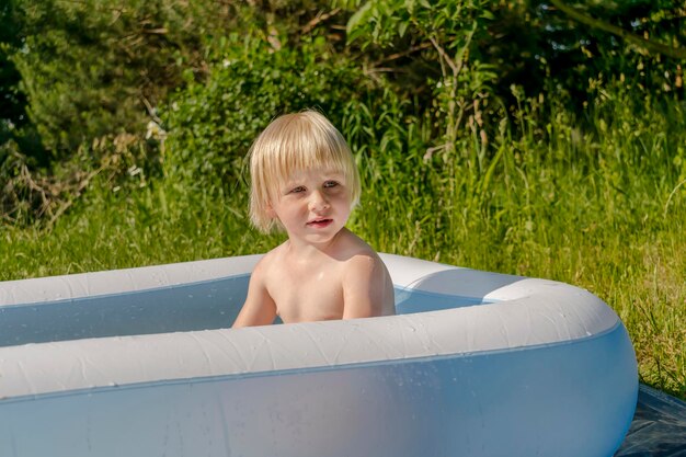 사진 귀여운 작은 유아 소년은 개인 주택 마을 자연 뒷마당에서 부풀어 오르는 수영장에서 재미있게 놀고 있습니다. 작은 아이들과 함께 여름 레크리에이션 휴가 휴가 어린이 건강 관리 시간