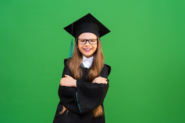 A cute adorable schoolgirl is very happy to study at school, a\
student in a master\'s gown and a hat is waiting for a certificate,\
a beautiful girl on a green isolated background with glasses,