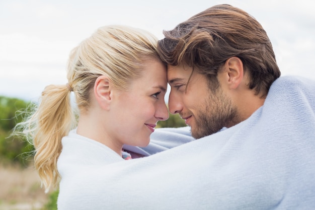 Cute affectionate couple standing outside wrapped in blanket