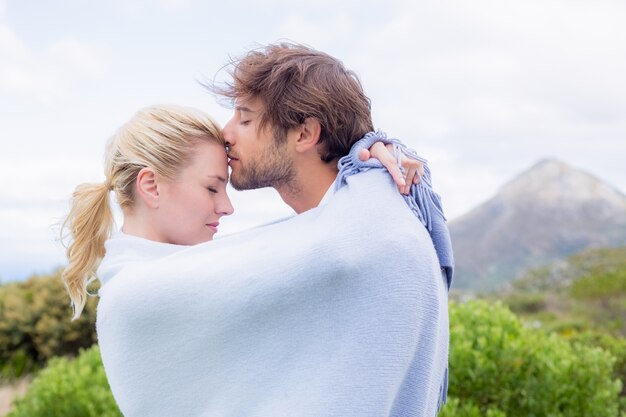 Cute affectionate couple standing outside wrapped in blanket