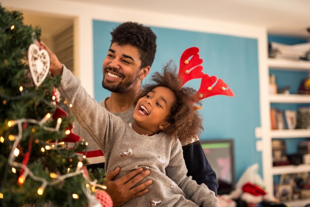 Cute african american girl decorating Christmas tree with dad