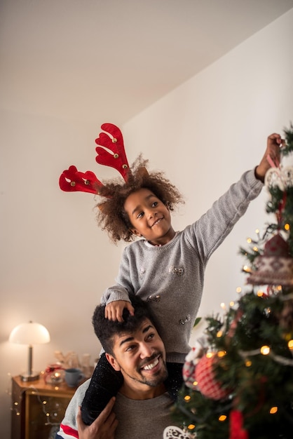 Cute african american girl decorating Christmas tree with dad