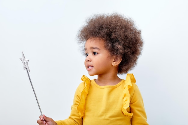 かわいいアフリカ系アメリカ人の女の子wth巻き毛のふわふわの髪の白いスタジオの壁に分離された魔法の杖を保持しています...