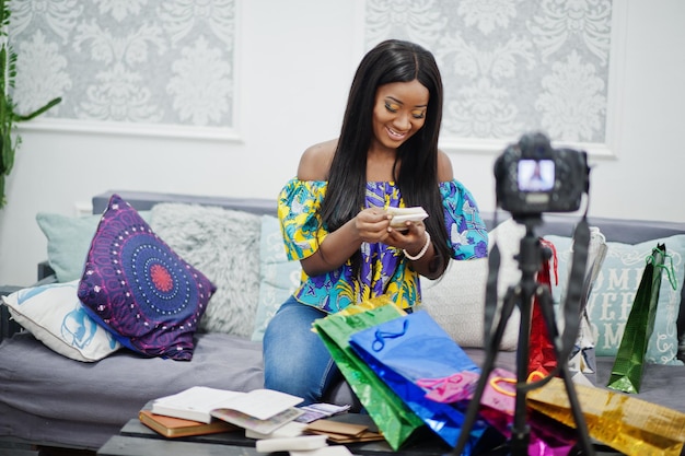 삼각대에 장착된 디지털 카메라를 사용하여 돈으로 블로그를 위한 비디오를 만드는 귀여운 아프리카계 미국인 여성 카메라에 젊은 여성 블로거 또는 동영상 블로거