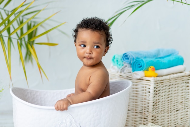 Cute African baby bathes and plays in the bath at home, the concept of care and hygiene for young children.