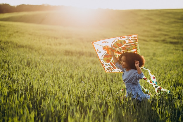 Cute african baby girl at the field on the sunset playing with kite