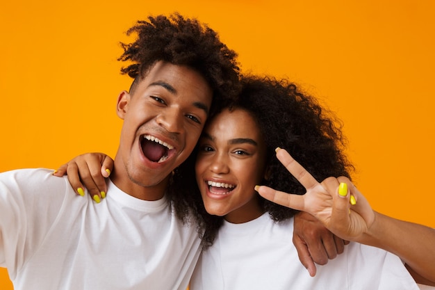 Cute african couple posing isolated over beige space showing peace gesture take a selfie by camera.