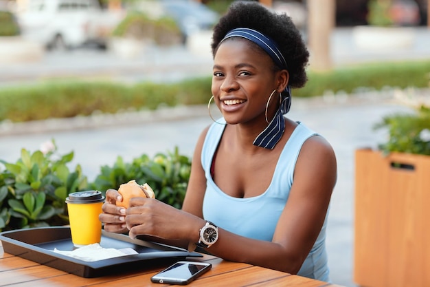アフリカ系アメリカ人の女性が笑顔で市内のカフェで外で昼食をとっている可愛いアフリカ人女性