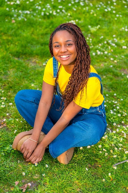 Cute african young woman in dungarees sitting on a park