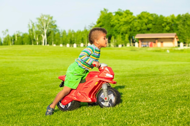 赤いバイクのおもちゃのかわいいアフロの男の子。