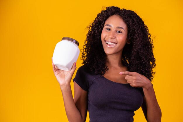 Cute afro girl with curly hair with a bottle of moisturizing\
cream afro woman with a moisturizing mask for afro hair