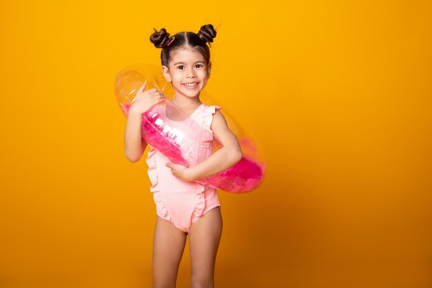 Cute arab little girl in swimming suit and swimming inflatable ring smiling having fun on yellow surface.