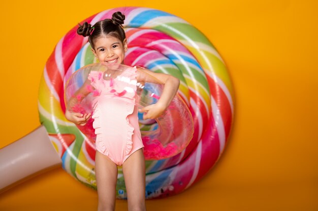 Cute arab little girl in swimming suit and swimming inflatable ring smiling having fun on yellow surface.