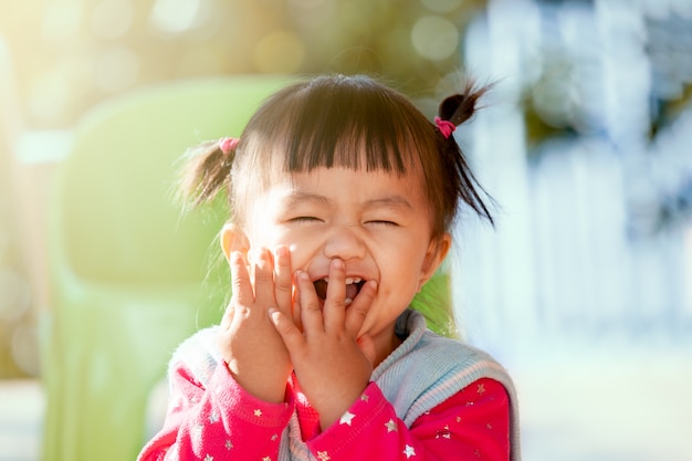 Neonata asiatica sveglia che ride e che gioca peekaboo o nascondino con divertimento