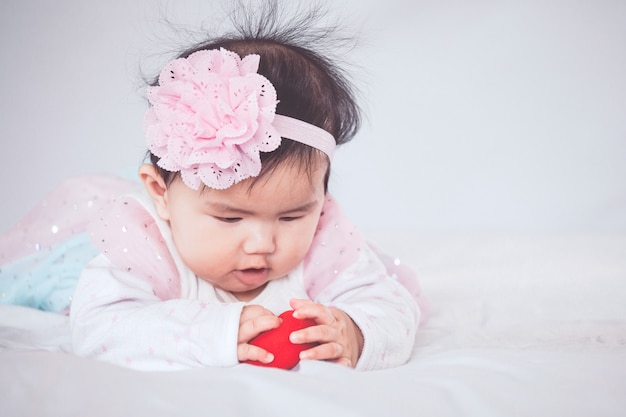그녀의 뱃속에 누워 침대에 그녀의 장난감을 가지고 노는 귀여운 아시아 여자 아기