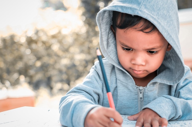 Cute Asian child drawing picture with crayon.