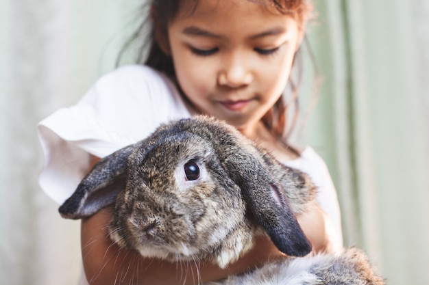 Cute asian child girl carrying and playing with cute holland rabbit with love and tenderness at easter festive