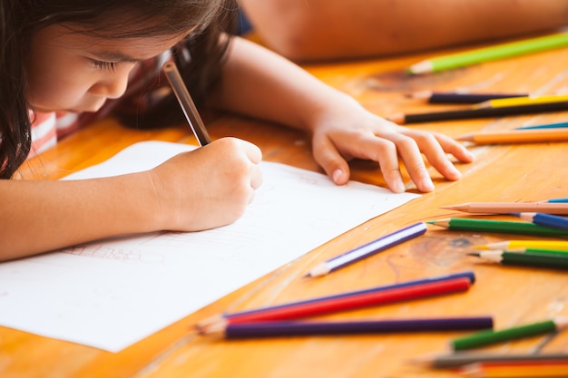 Foto ragazza asiatica sveglia del bambino che disegna e che dipinge con il pastello con divertimento