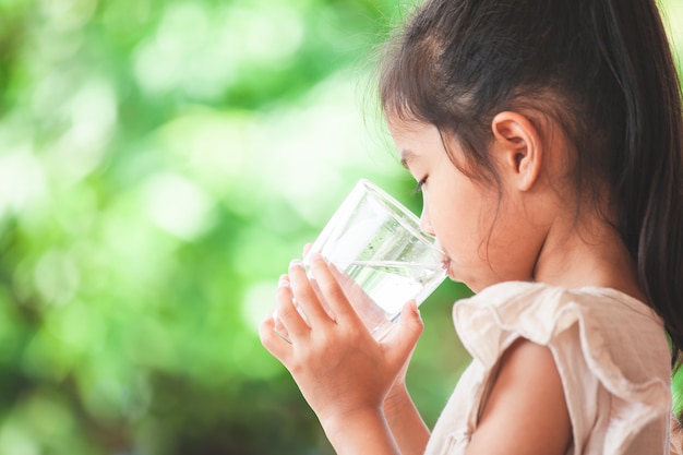 Cute asian child girl drinking fresh water from glass 