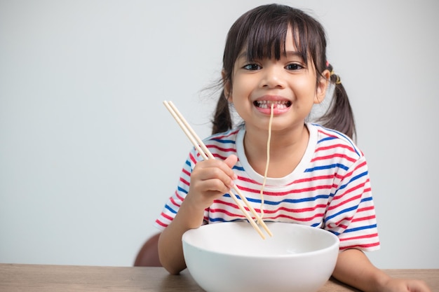 Cute Asian child girl eating delicious instant noodles at home