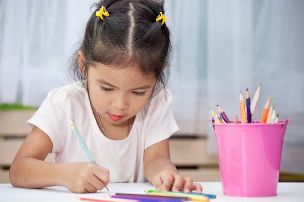 Cute asian child girl having fun to draw and paint with crayon 