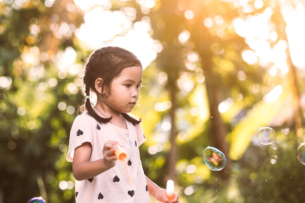 夕日に屋外で泡で遊ぶのが楽しいかわいいアジアの子供の女の子