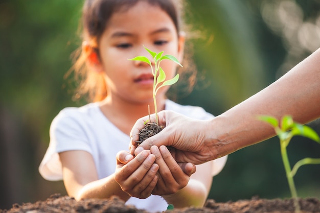 かわいいアジアの子少女と親が庭で一緒に黒い土に若い苗を植える