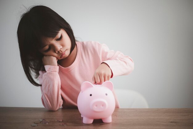 Cute asian child girl putting money into piggy bank to save money for the future