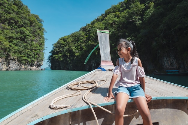 Ragazza asiatica sveglia del bambino che si siede sulla testa della barca di legno di longtail.