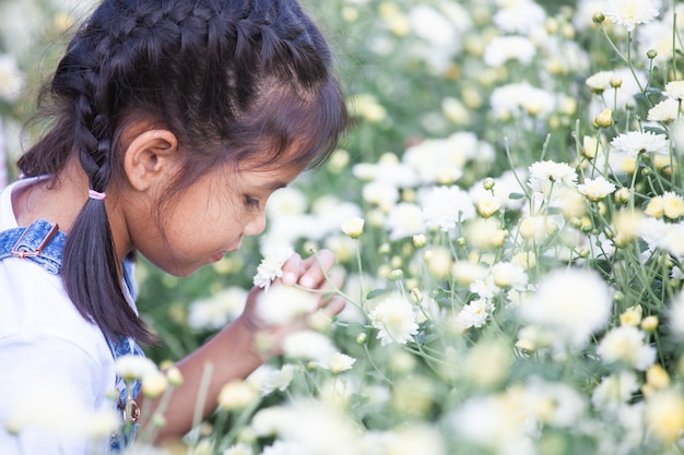 Cute asian child girl sniffing beautiful flower in the flower field with happiness