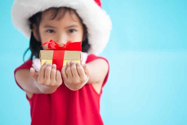 Cute asian child girl wearing santa hat and holding beautiful gift in hand 