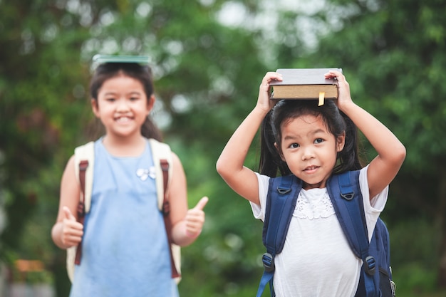 학교 가방과 그녀의 여동생과 함께 귀여운 아시아 아이 소녀는 함께 머리에 책을 넣어